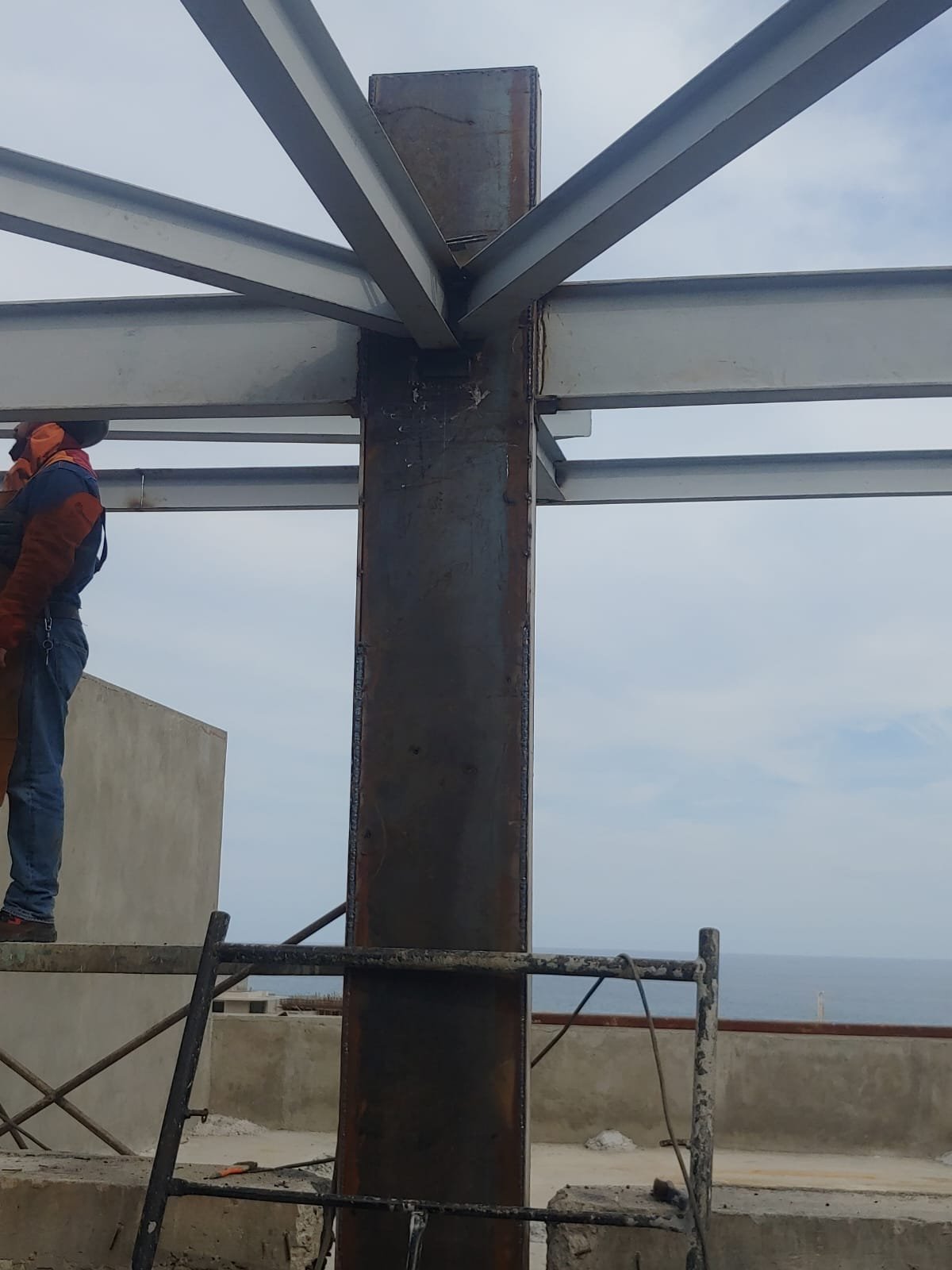 Columna de acero con vigas convergentes y soldador en andamio